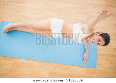 Fit woman doing a side plank and smiling at camera at home on wooden floor