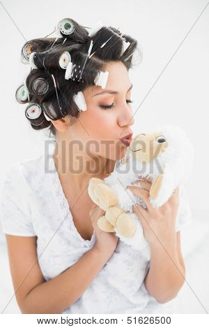 Brunette in hair rollers kissing sheep teddy  at home in bedroom