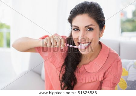 Cheerful brunette sitting on her sofa brushing her teeth at home in the sitting room