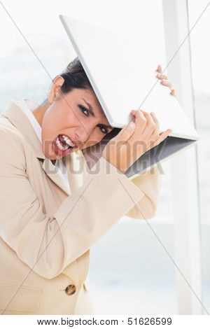 Crazed businesswoman hitting head off laptop looking at camera in her office