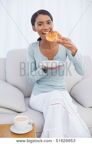 Cheerful attractive woman having a breakfast sitting on cosy sofa