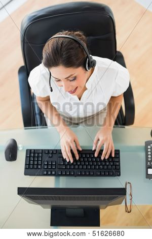 Pretty call center agent typing while on a call in her workplace