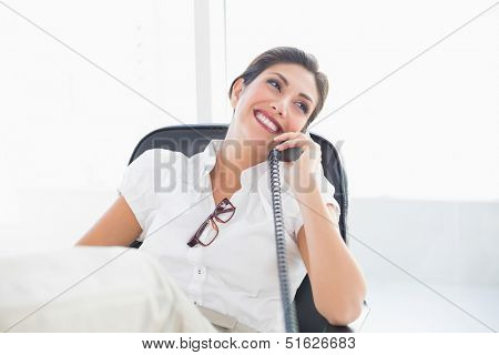 Reclining businesswoman sitting at her desk talking on phone in her office