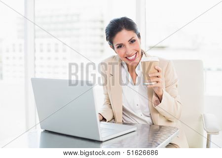 Happy businesswoman drinking coffee while working on laptop at the office