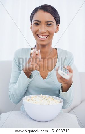 Cheerful attractive woman sitting on cosy sofa eating popcorn while watching tv