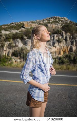 Stylish woman enjoying the sunshine against a mountain on a deserted road