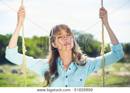 Natural attractive blonde sitting on swing in summertime