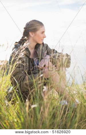 Blonde woman sitting in grass looking away in the countryside