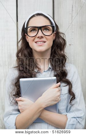 Pensive trendy woman with stylish glasses holding her tablet posing on wooden background