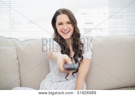 Smiling young woman changing tv station sitting on a cosy couch