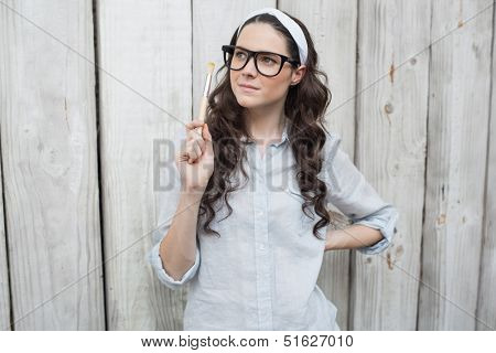 Artistic trendy woman with stylish glasses posing holding paintbrush on wooden background