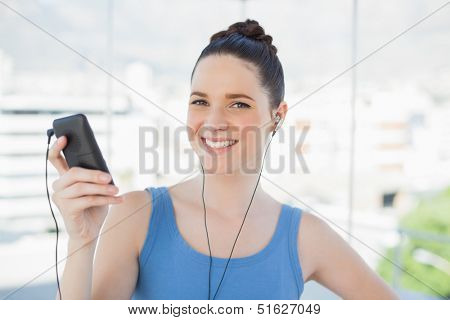 Smiling slender woman listening to music while exercising in bright sports hall