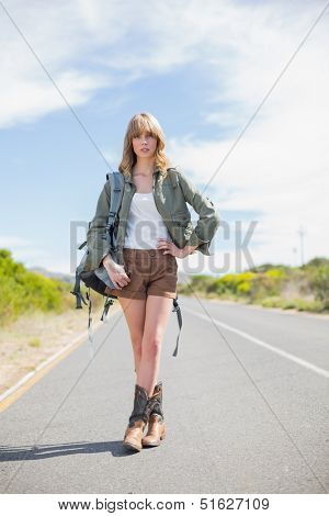 Sexy blonde woman posing while hitchhiking on a deserted road in summertime