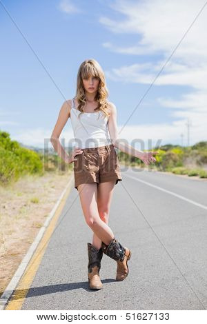 Mysterious attractive woman posing while hitchhiking on a deserted road in summertime