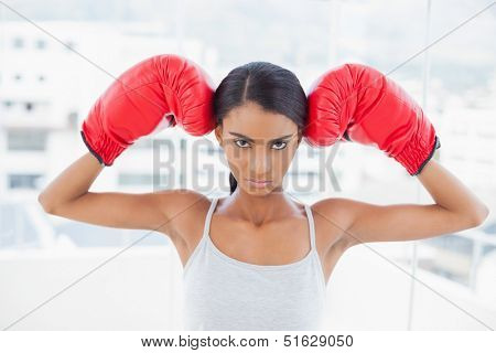Serious competitive model in bright room at home wearing red boxing gloves