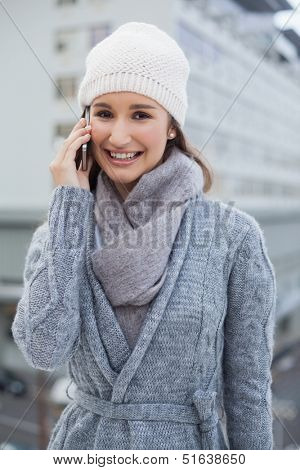 Cheerful gorgeous woman wearing winter clothes having a call outdoors on a cold grey day