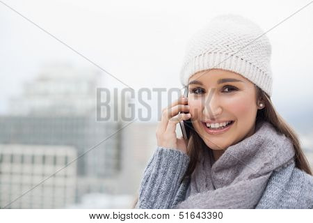 Smiling brunette with winter clothes on having a call outdoors on a cold grey day