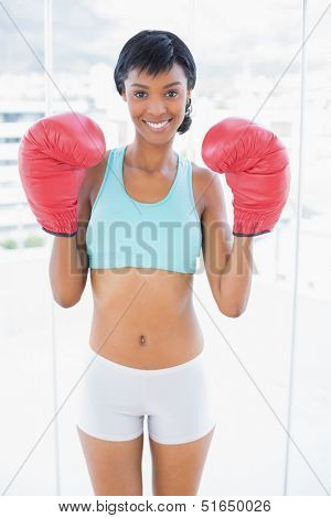 Smiling black haired woman wearing boxing gloves in a living room