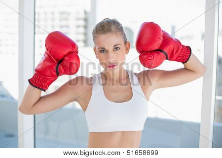 Dynamic young blonde model in white sportswear wearing boxing gloves