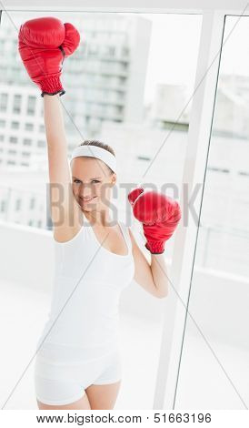 Cheering pretty sportswoman raising her boxing glove in a bright room