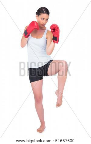 Healthy model with boxing gloves kicking while posing on white background