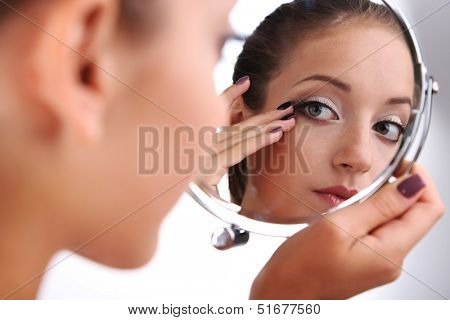 Beautiful girl preens before small mirror isolated on white