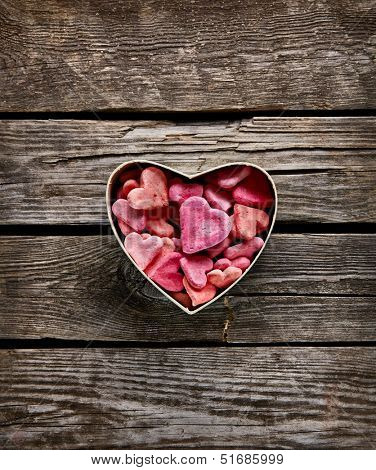 Open heart shaped Valentines Day gift box with heap of small hearts inside on old wooden background.