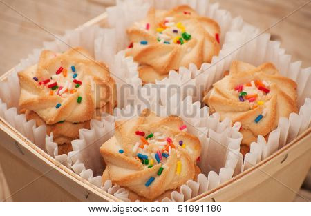 Closeup of shortbread cookies with colorful nonpareil sprinkles on top, in a wooden basket