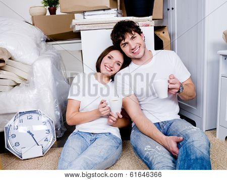 Happy people sitting on the floor with cups of tea after removing in the new home and relax