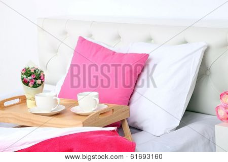 Cups of coffee on comfortable soft bed with pillows