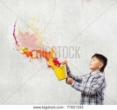Young boy splashing colorful paint from bucket