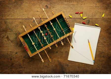 Mini soccer game and a blank note pad, on an old wooden table. Tactics, game planning concept. 