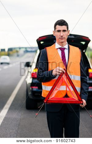 Man with car breakdown erecting warning triangle on road
