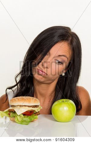 a young woman can not decide between a hamburger and an apple itself. healthy or unhealthy diet.