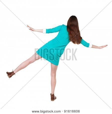 Back view woman Balances waving his arms.    backside view of person.  Isolated over white background. The girl in a blue dress with brown shoes keeps the balance standing on one leg.