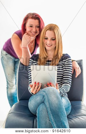 Two young women in jeans holding a tablet over white background