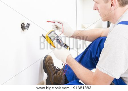 Electrician checking socket voltage with digital multimeter