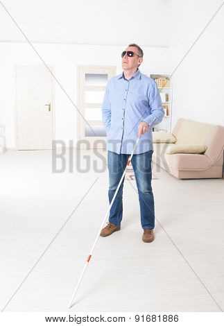 Blind man with white stick and dark glasses at home