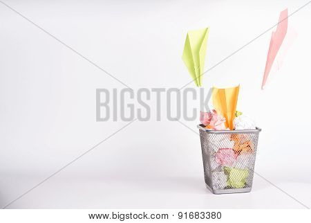 isolated wastebasket full of color waste paper and paper airplanes
