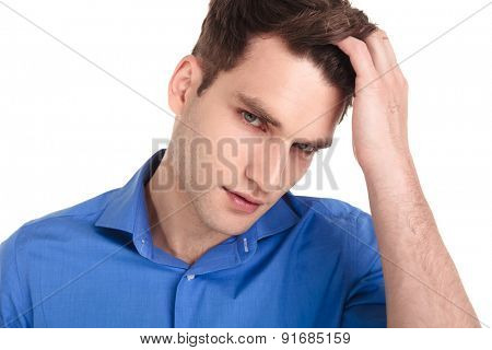 Close up picture of a handsome young man crossing his finger throungh his hair, looking at the camera.