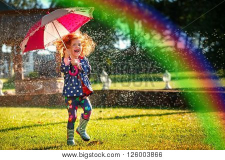 Laughing girl in the rain under umbrela with a rainbow.