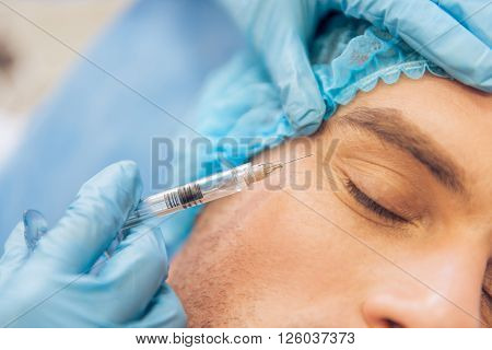 Portrait of handsome young man getting an injection in face lying with closed eyes close-up