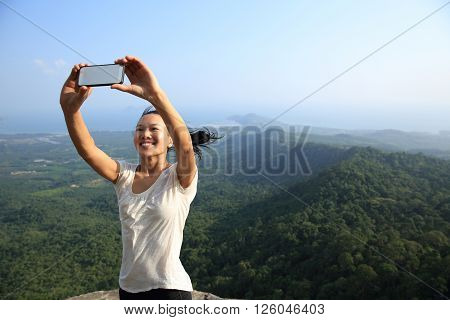 young asian woman taking photo with smart phone at mountain peak cliff