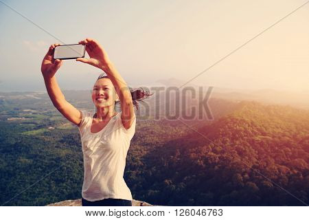 young asian woman taking photo with smart phone at mountain peak cliff