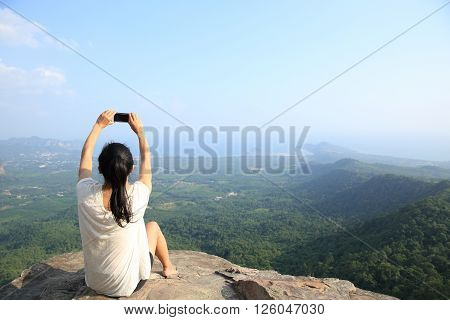 young asian woman taking photo with smart phone at mountain peak cliff