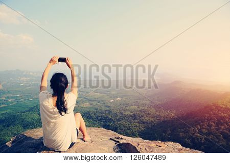 young asian woman taking photo with smart phone at mountain peak cliff