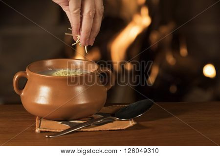 Serving Parmesan Cheese on a Bowl of Warm Soup / Hand serving parmesan cheese on a bowl of warm soup with a fireplace on the background
