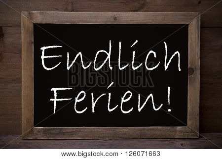 Brown Blackboard Or Chalkboard With German Text Endlich Ferien Means Happy School Vacation As Greeting Card. Wooden Background. Vintage Rustic Style.