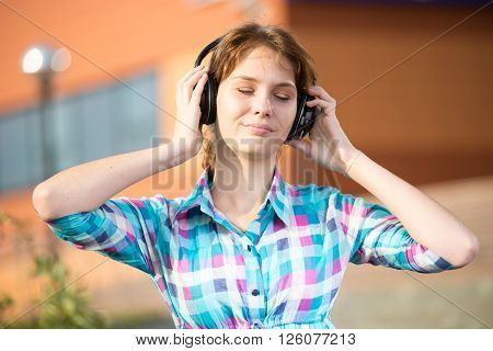 Young beautiful girl listening to music player on the street. tudent woman at campus park.