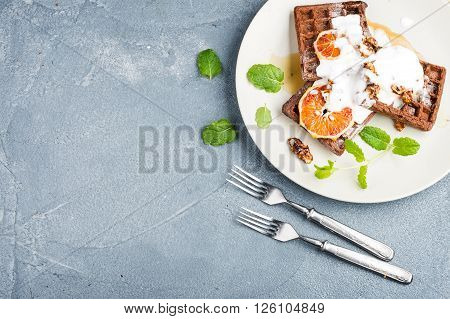 Belgian soft waffles with blood orange, cream, marple syrup and mint  on white plates over concrete textured background. Top view, copy space